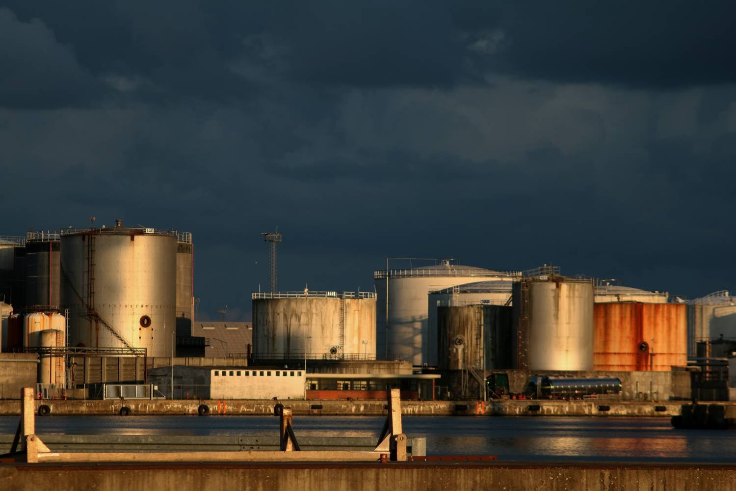 Oil storage tanks lit by evening light under a dark sky
